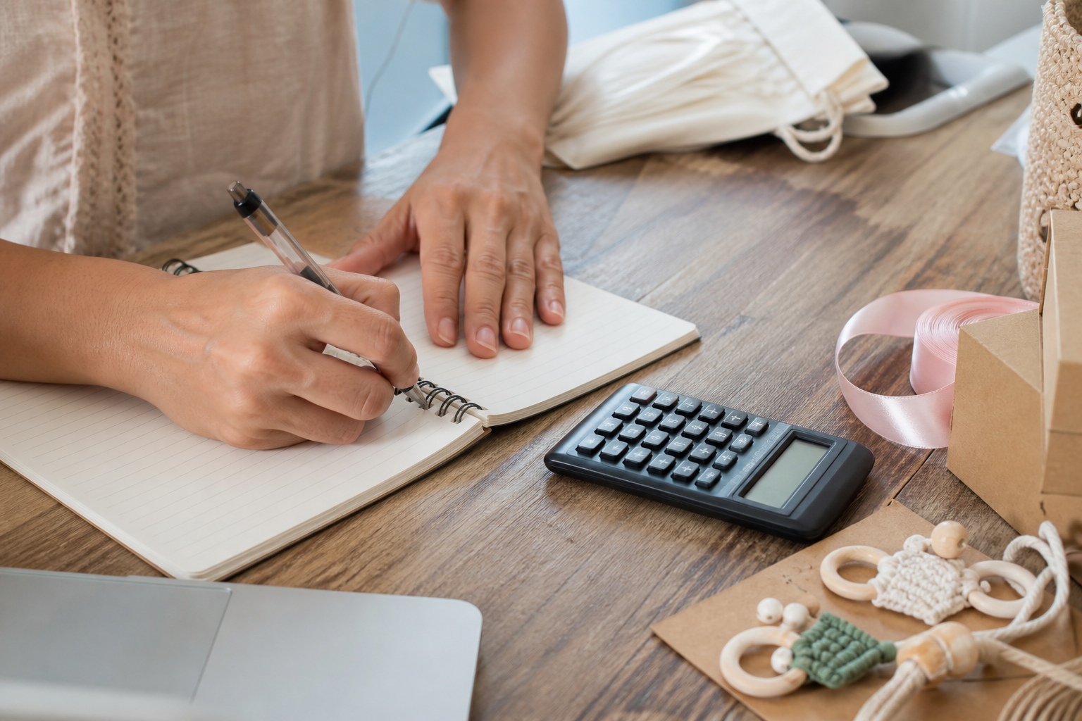 Mãos calculando custos e preço de uma pequena produção artesanal